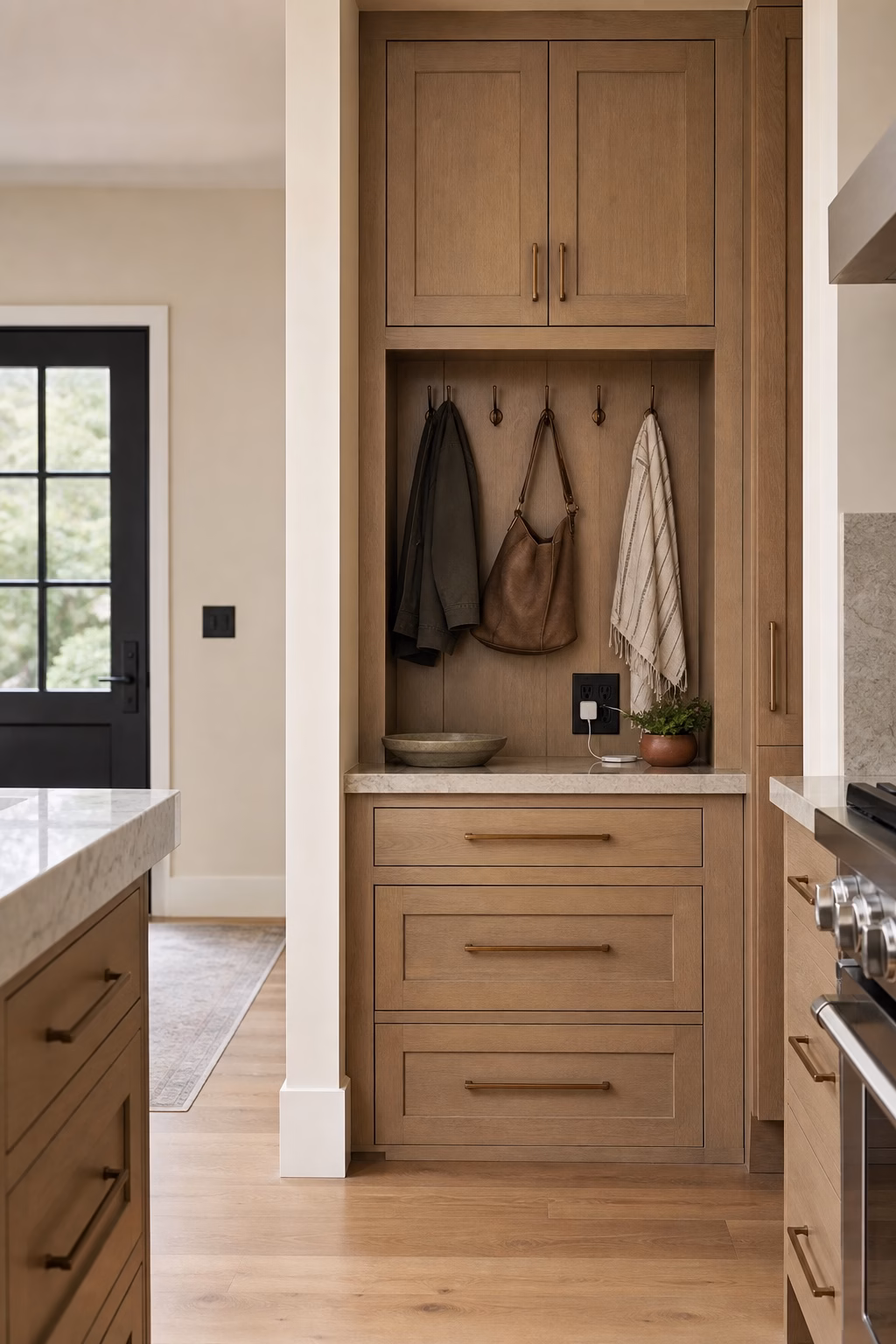 Kitchen entry drop zone with shallow drawers, hooks, charging outlet, wood cabinetry, and clear island