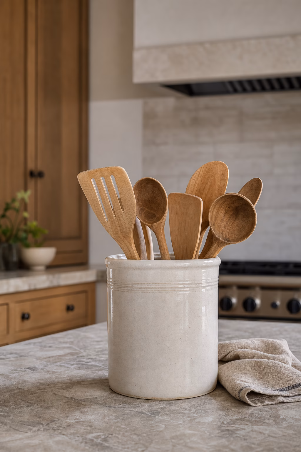 Cream ceramic utensil crock holding wooden spoons and spatulas on a stone island