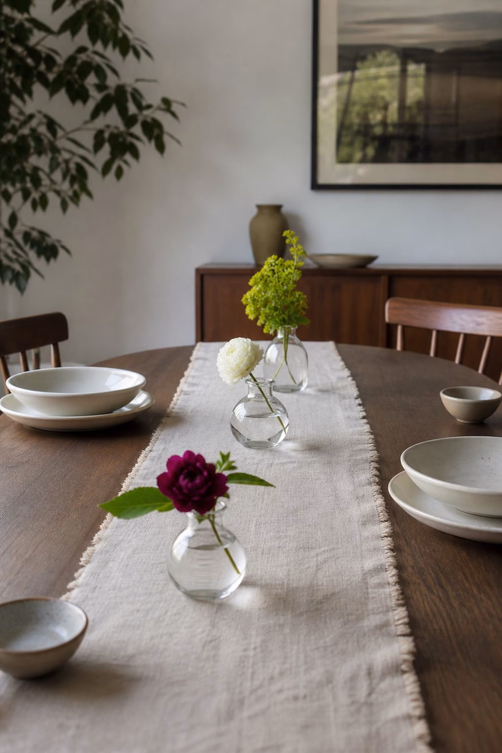 Three bud vases displaying small fresh flower stems on a dining table