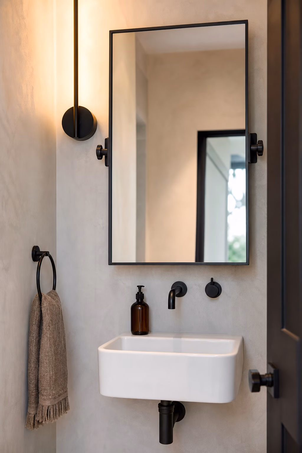 Black pivot bathroom mirror above a small wall mounted sink in a narrow powder room