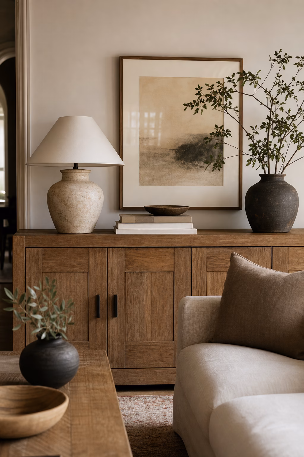 Neutral living room console styled with ceramic lamp books bowl and framed art