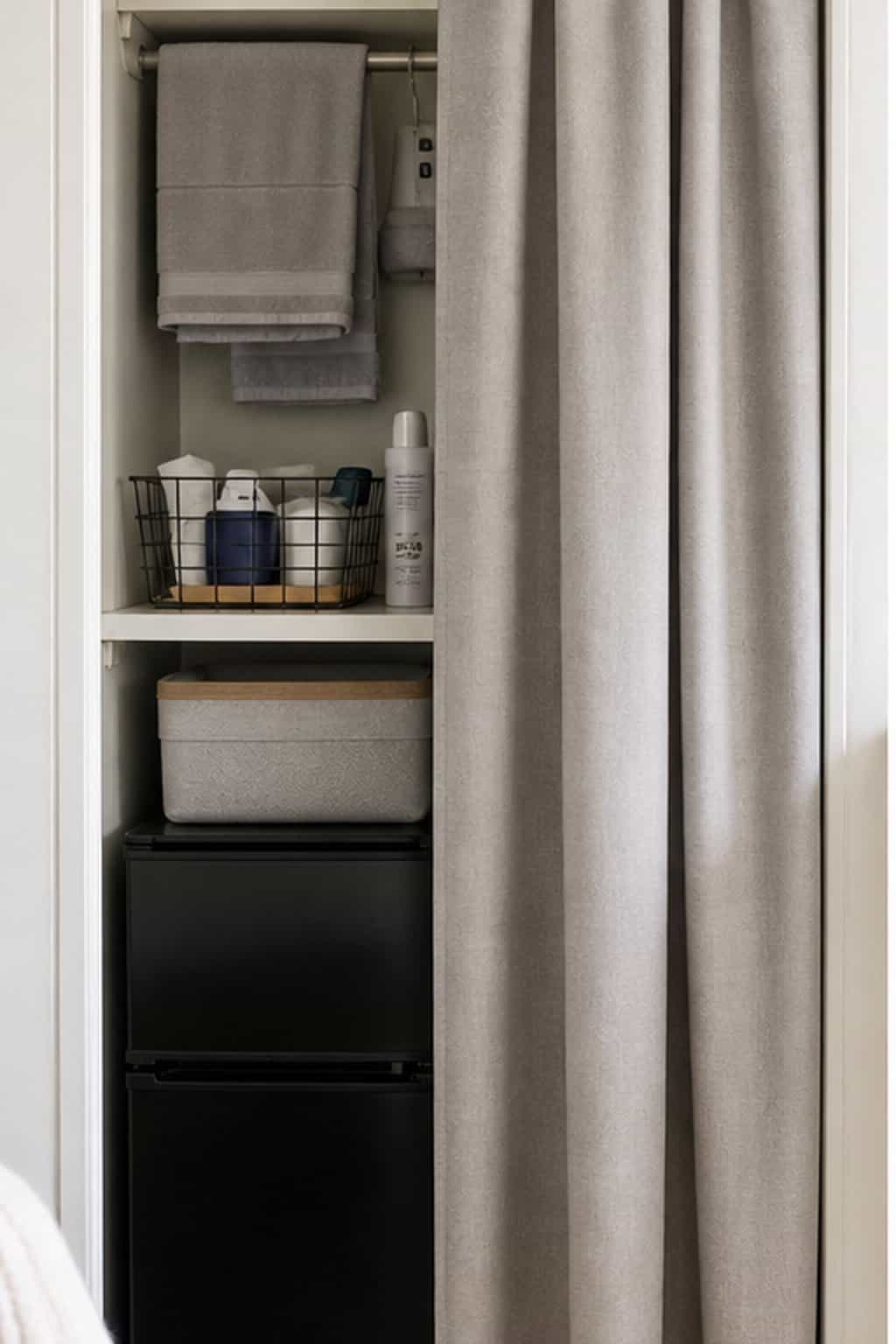 Dorm utility storage hidden behind a neutral tension-rod curtain for a cleaner look.