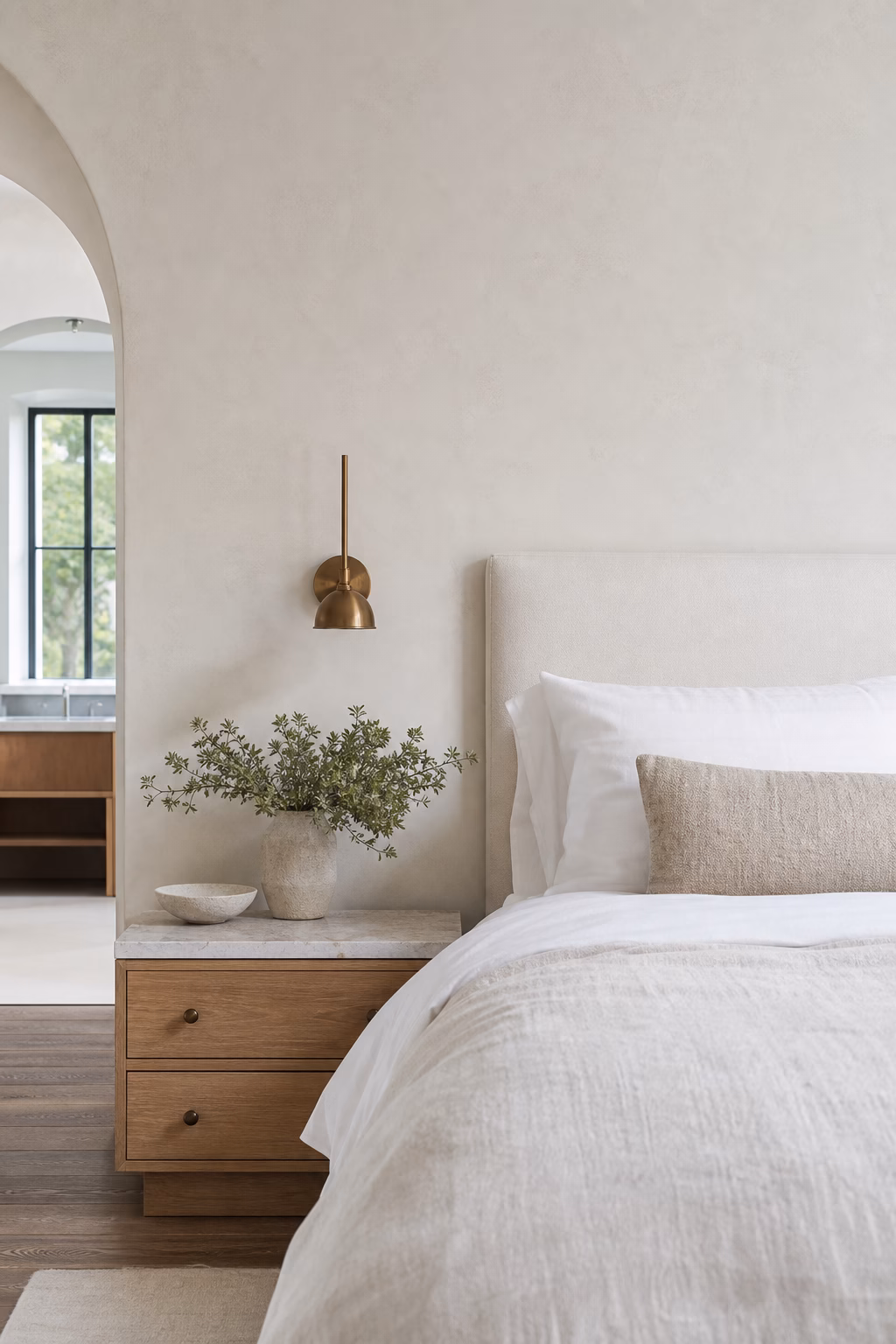 White bedroom with matte plaster walls, honed stone, brushed metal sconces, and linen bedding.