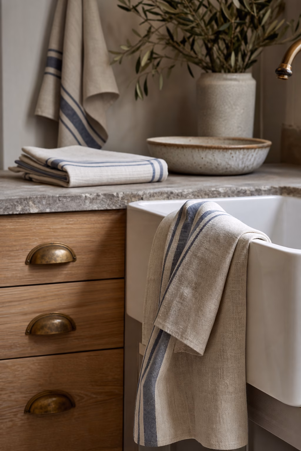 Striped linen kitchen towels folded and hanging beside a farmhouse sink