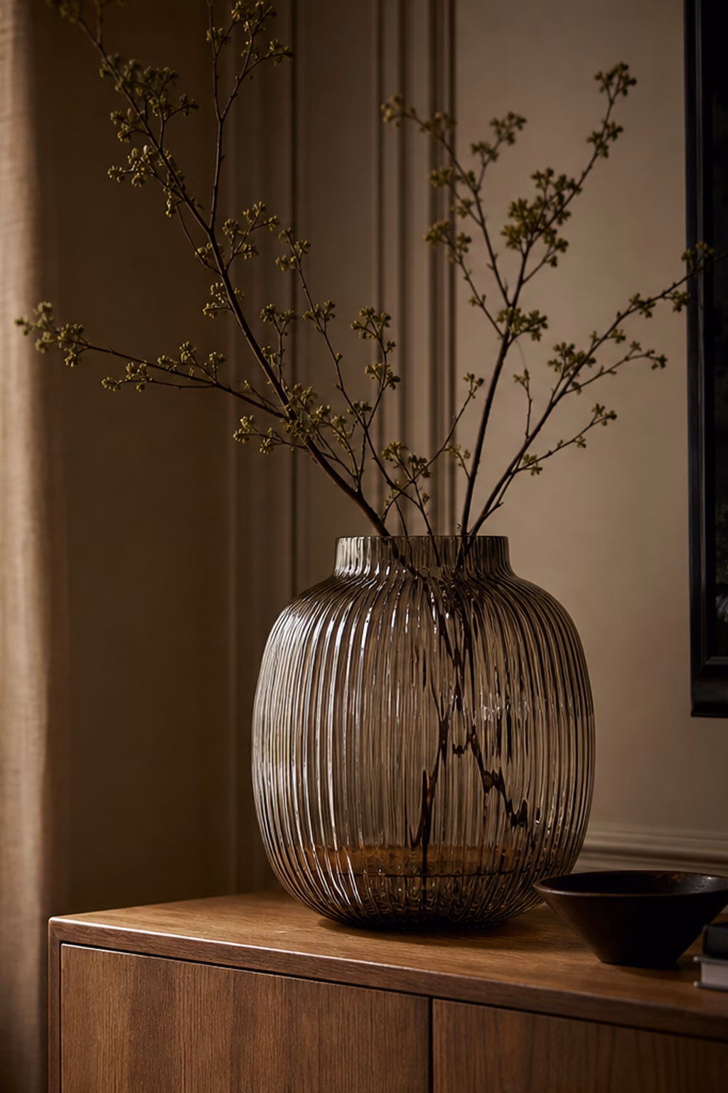Ribbed glass vase with branches styled on a wood console.