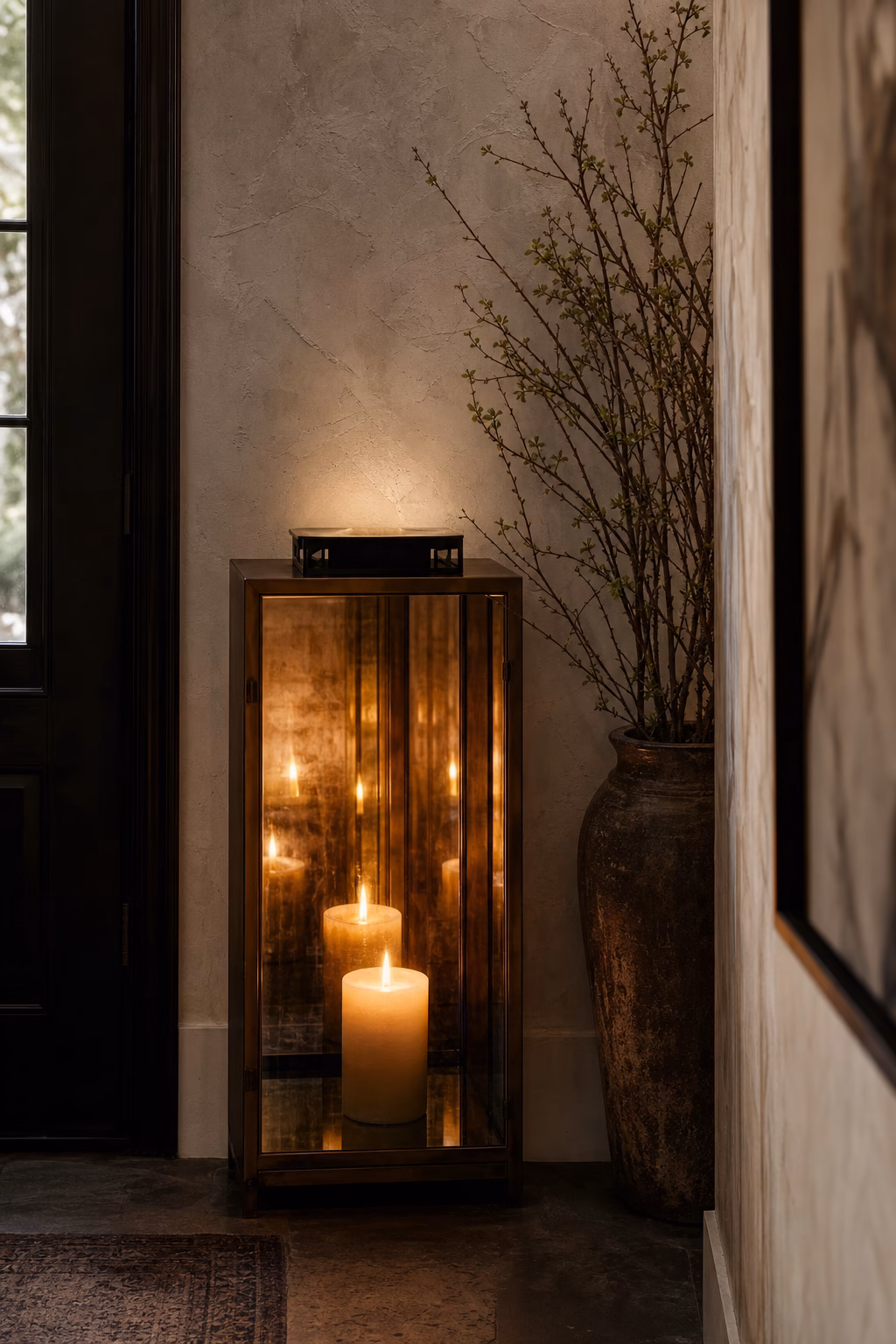 Smoked mirrored lantern reflecting candlelight in a compact entry niche