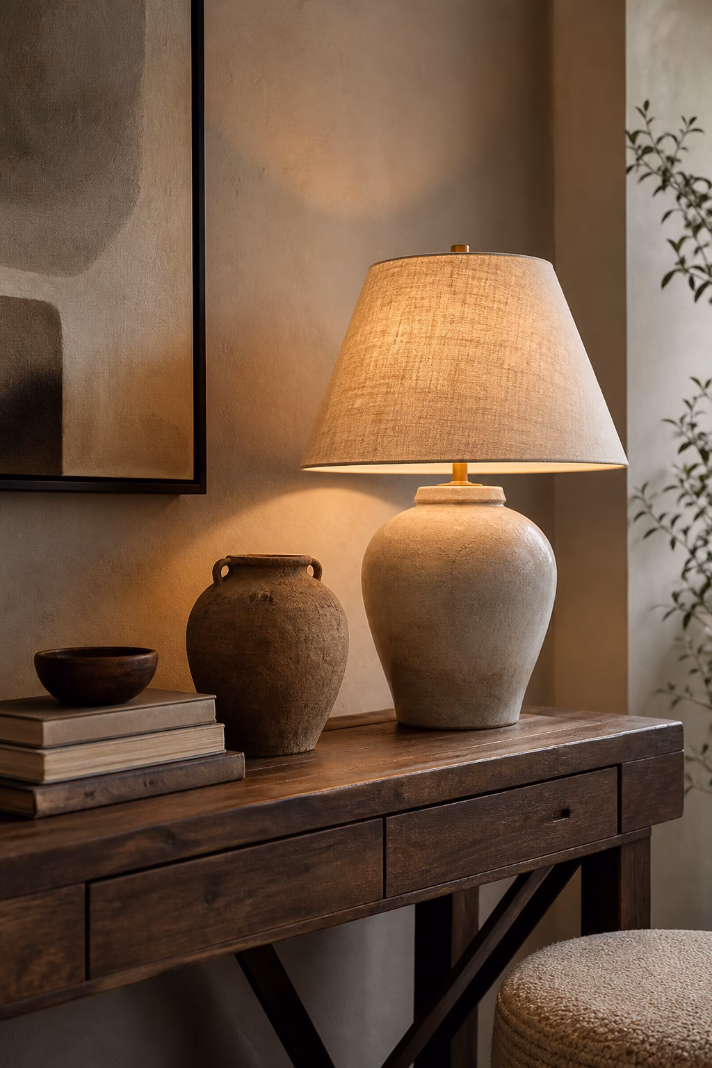 Ceramic table lamp on a wood console below framed art with warm shade glow