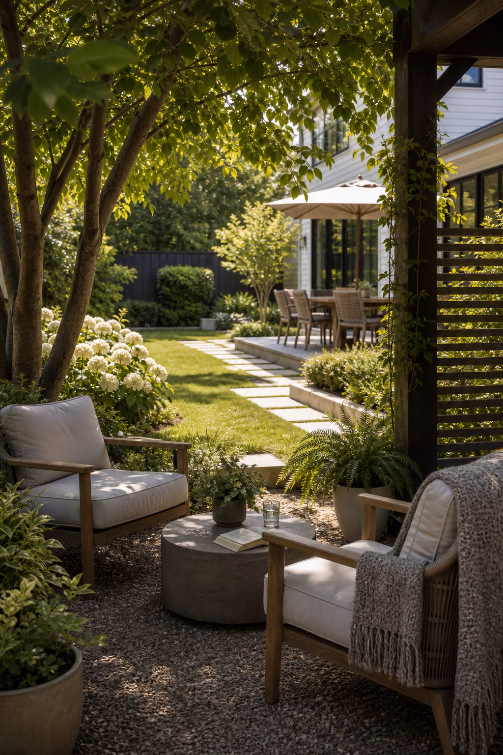 Quiet shaded backyard reading corner with outdoor chairs, small table, and view toward lawn.