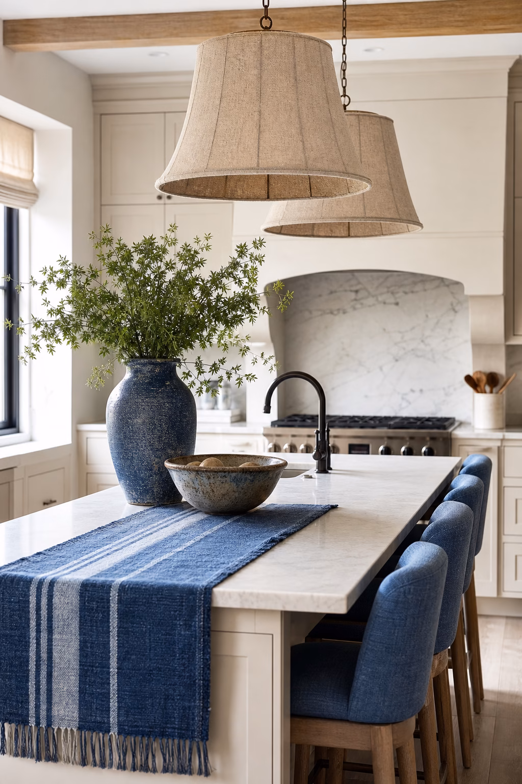 Neutral kitchen styled with blue textiles, ceramics, and upholstered stools.
